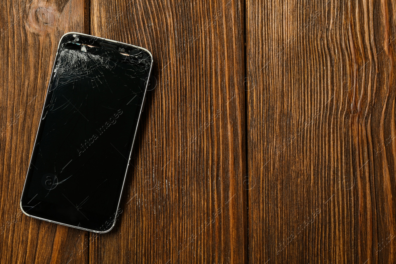 Photo of Damaged smartphone on wooden table, top view with space for text. Device repairing