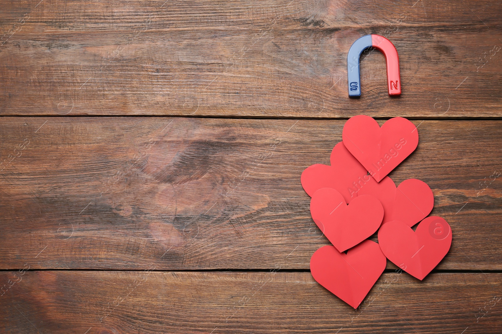 Photo of Magnet attracting red hearts on wooden background, top view with space for text. Love concept