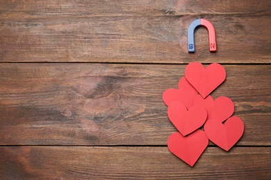 Photo of Magnet attracting red hearts on wooden background, top view with space for text. Love concept