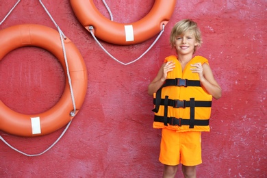 Photo of Little boy wearing orange life vest near red wall with safety rings