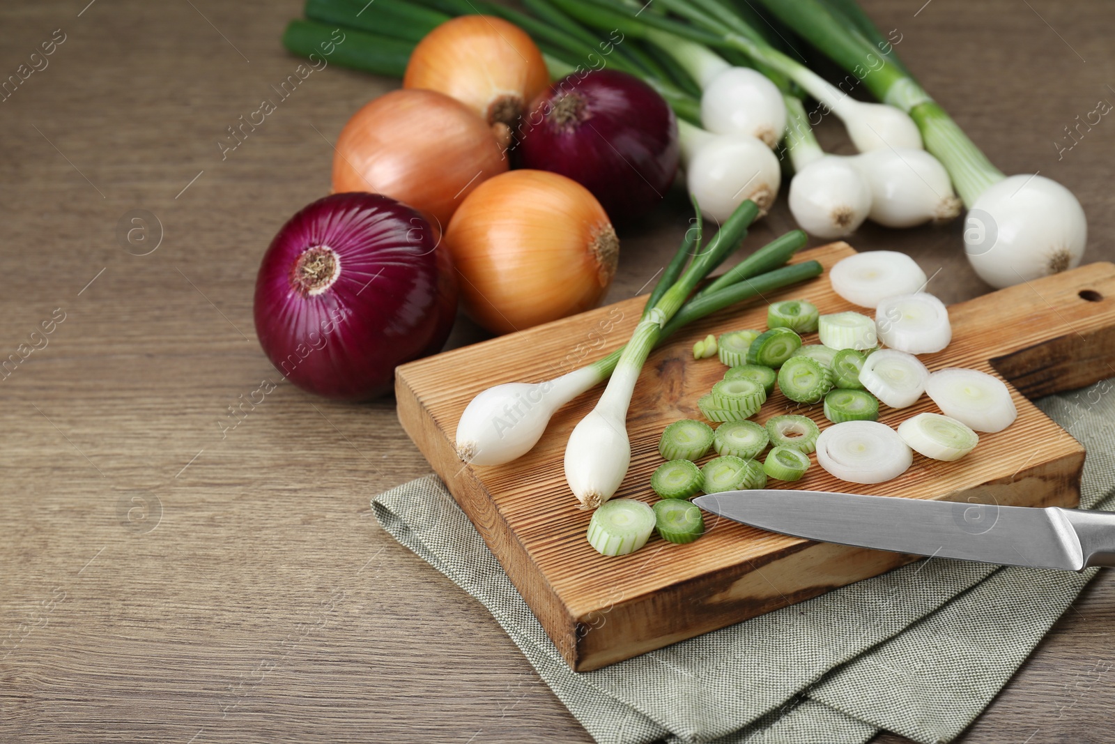 Photo of Different kinds of onions on wooden table, closeup. Space for text