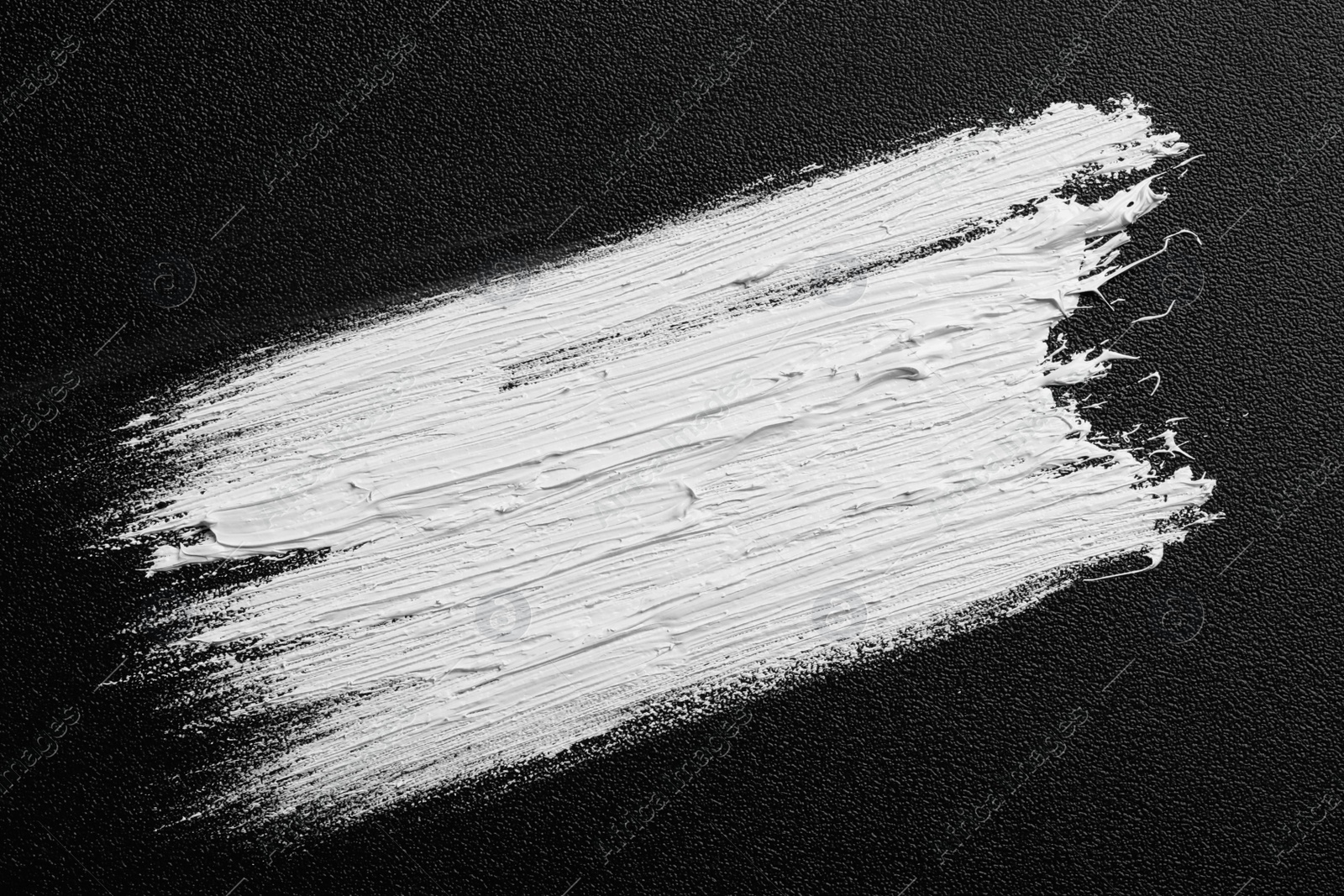 Photo of Strokes of white oil paint on black canvas, top view