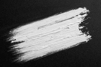 Photo of Strokes of white oil paint on black canvas, top view