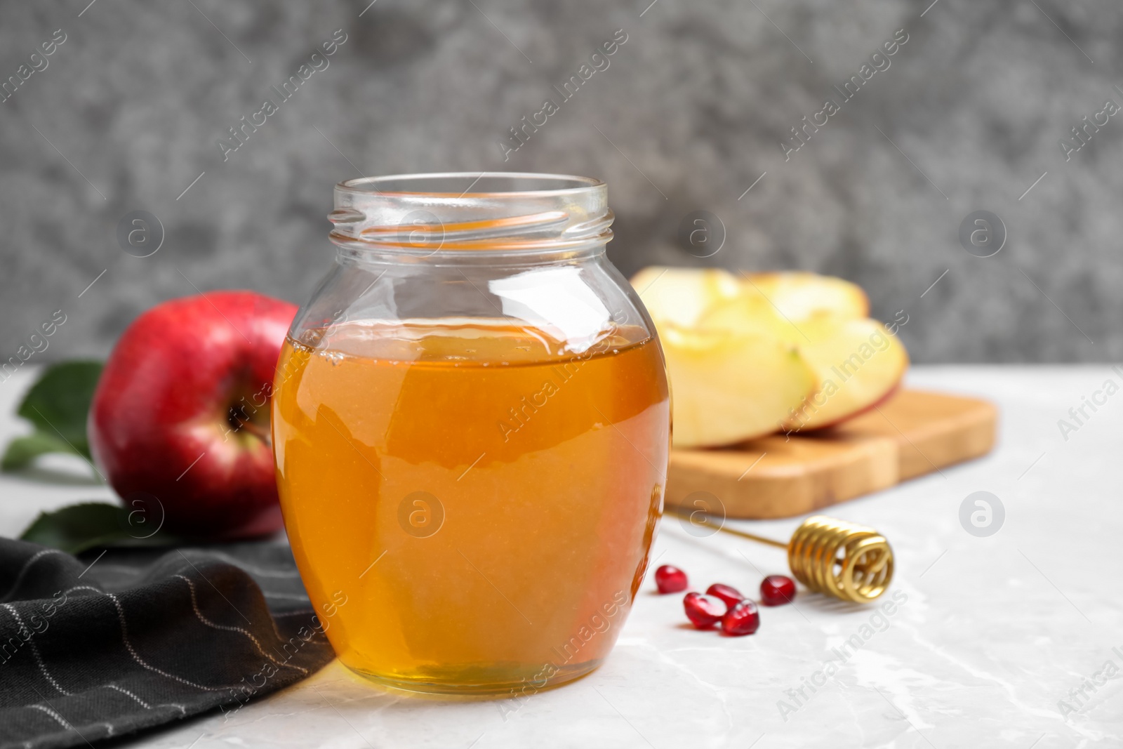 Photo of Honey, pomegranate seeds and apples on light grey marble table. Rosh Hashanah holiday