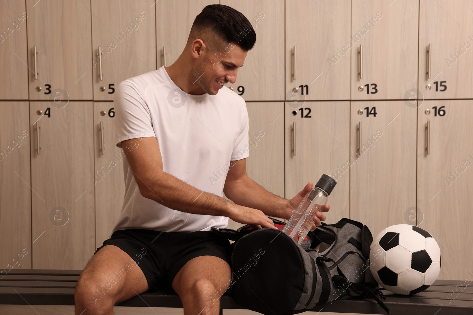 Photo of Handsome man taking bottle from sports bag in locker room