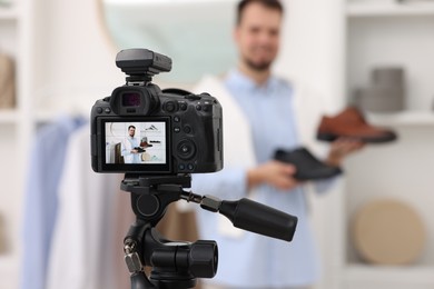 Photo of Fashion blogger showing shoes while recording video at home, focus on camera