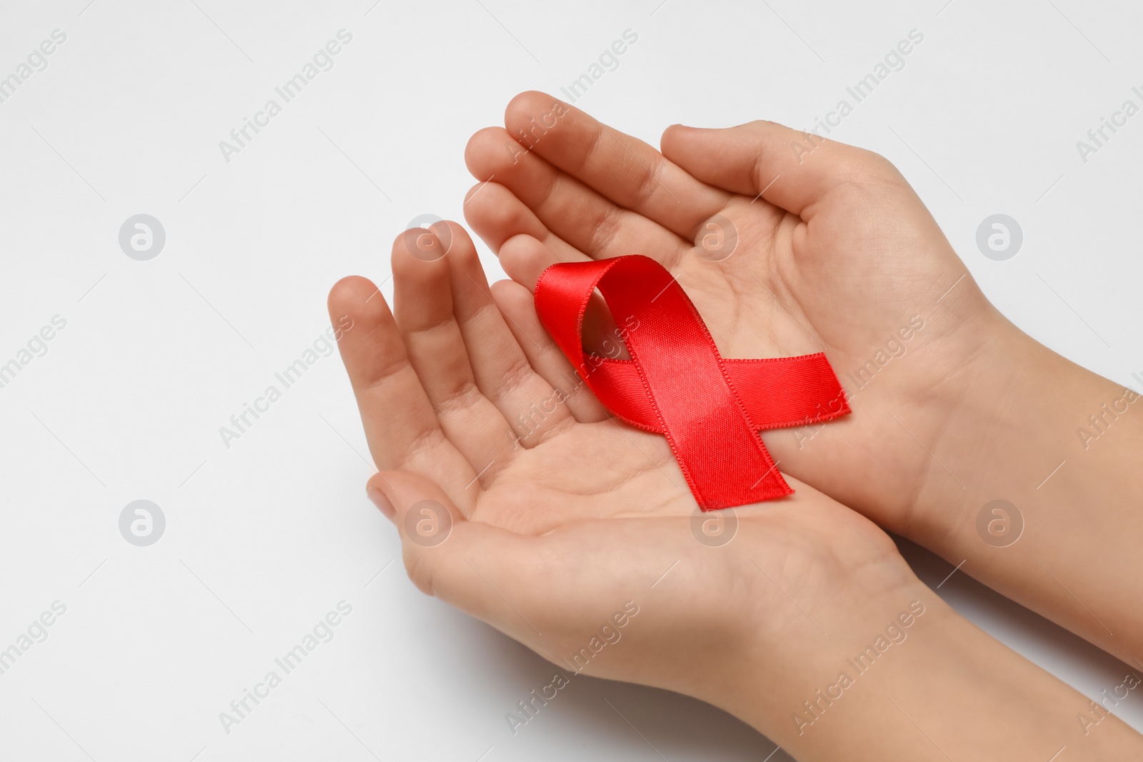 Photo of Little girl holding red ribbon on white background, closeup. AIDS disease awareness