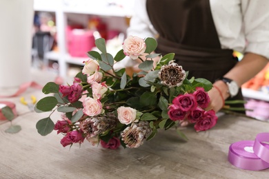 Photo of Female florist with bouquet of beautiful flowers at table in shop