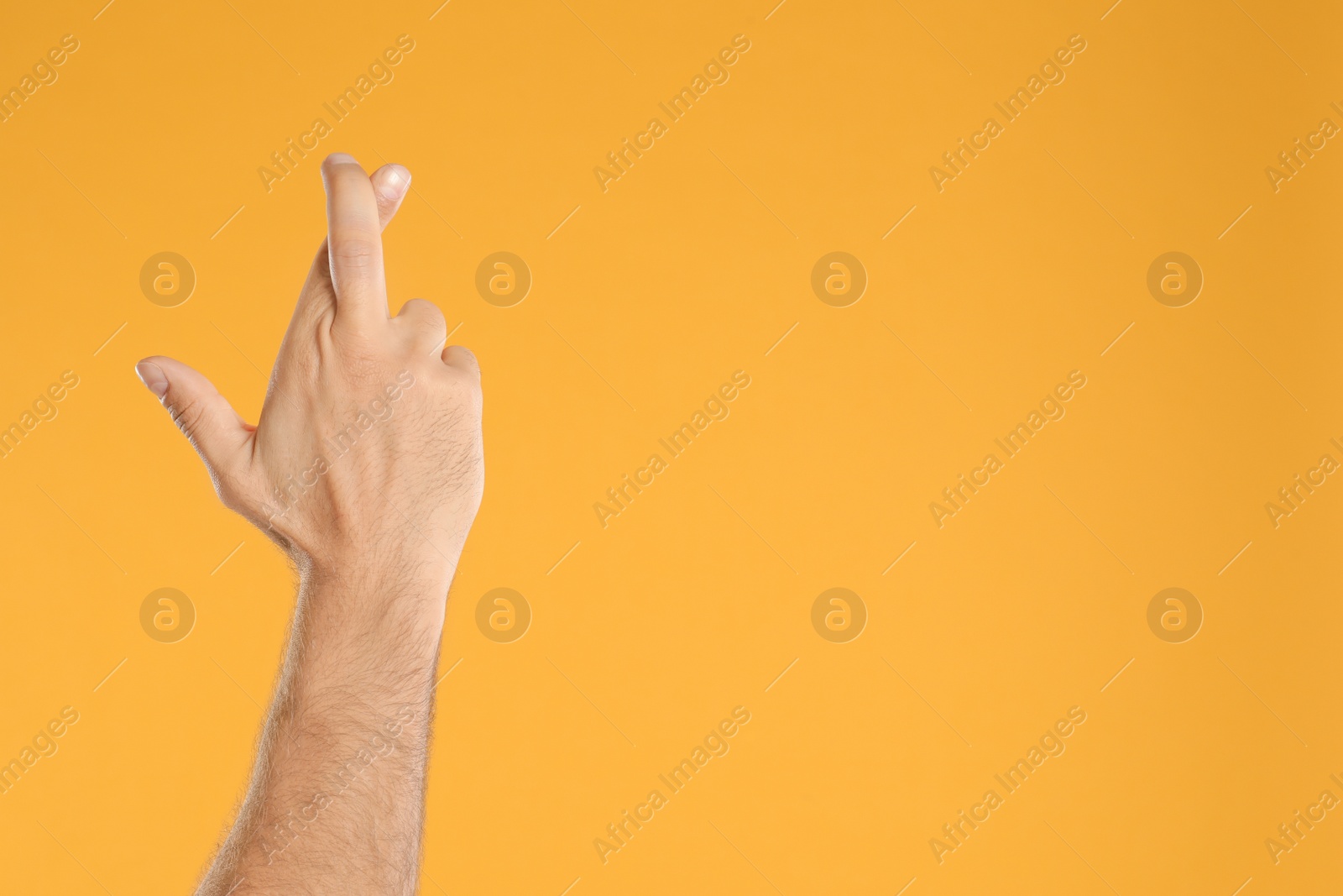 Photo of Man with crossed fingers and space for text on yellow background, closeup. Superstition concept