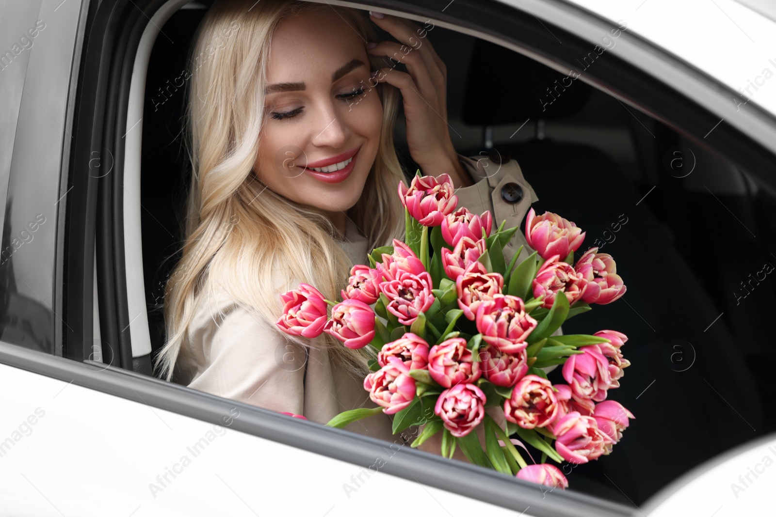 Photo of Happy young woman with beautiful bouquet in car