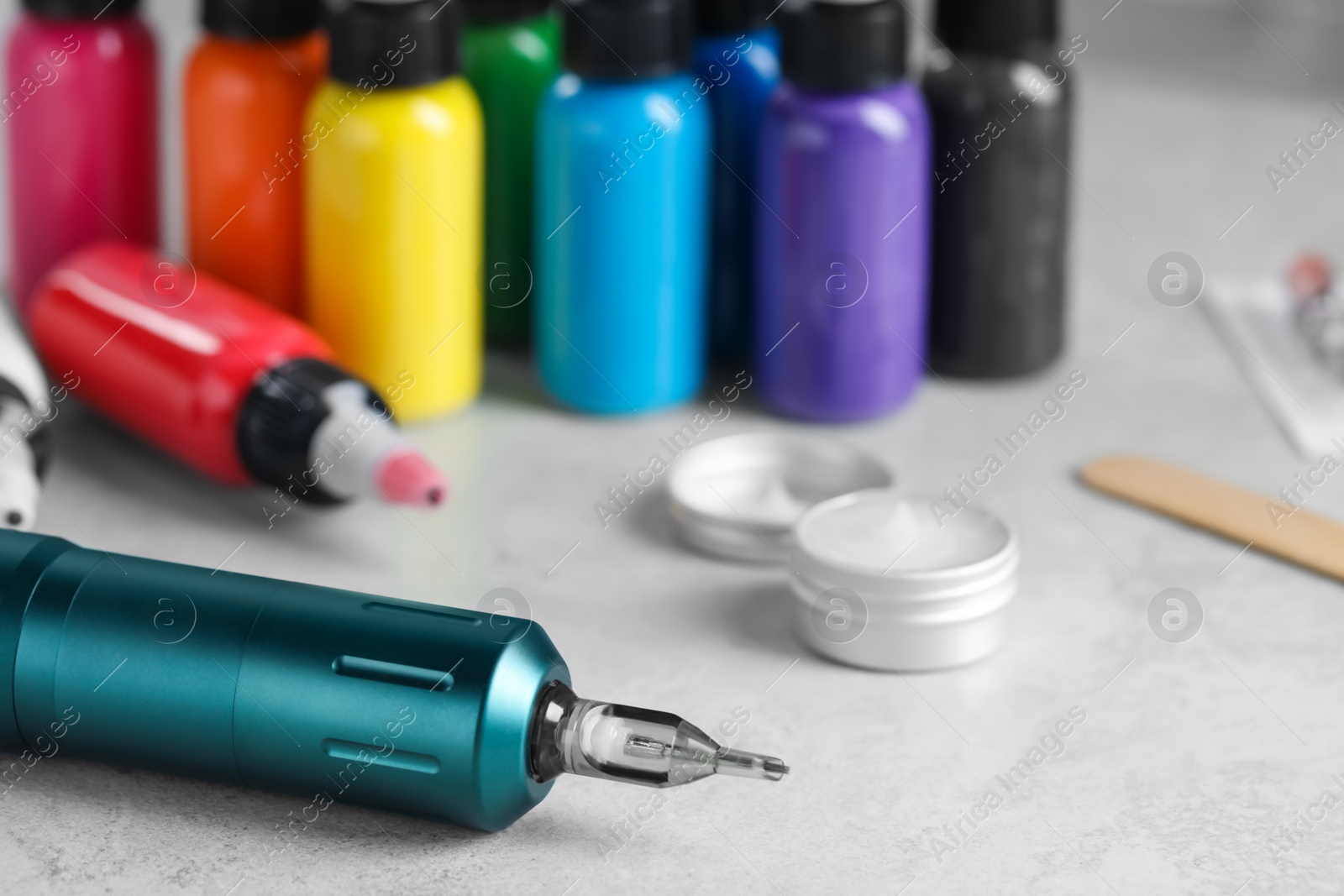 Photo of Modern professional tattoo machine and colorful inks on white table, space for text