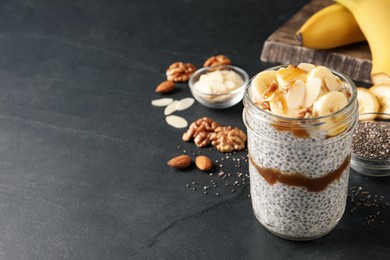 Photo of Delicious chia pudding with banana, walnuts and caramel sauce on black table, space for text