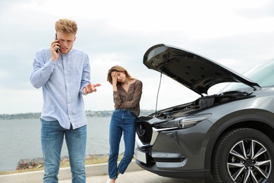 Photo of Young man and woman near broken car outdoors