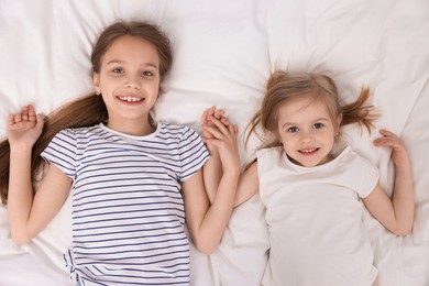 Photo of Cute little sisters on bed, top view