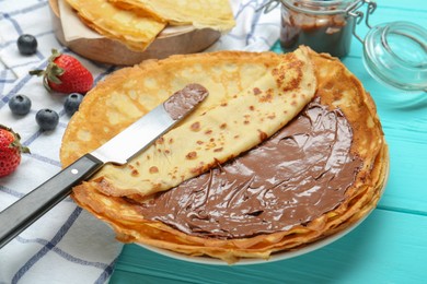 Photo of Tasty crepes with chocolate paste and berries served on turquoise wooden table, closeup