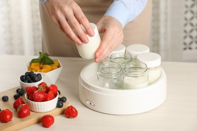 Photo of Woman making tasty yogurt at white wooden table in kitchen, closeup