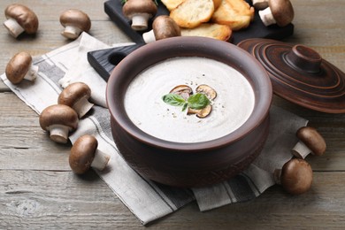 Photo of Delicious homemade mushroom soup in ceramic pot and fresh ingredients on wooden table