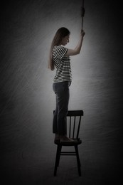 Image of Depressed woman with rope noose standing on chair against grey background. Suicide concept