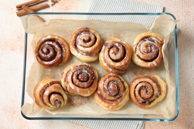 Photo of Baking dish with tasty cinnamon rolls on beige textured table, top view