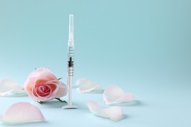 Photo of Cosmetology. Medical syringe, rose flower and petals on light blue background, space for text