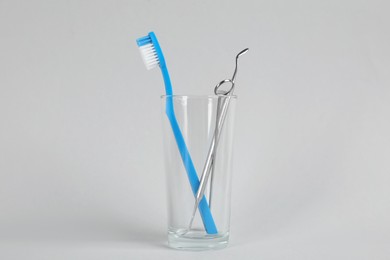 Photo of Glass holder with toothbrush and dentist's tools on light grey background