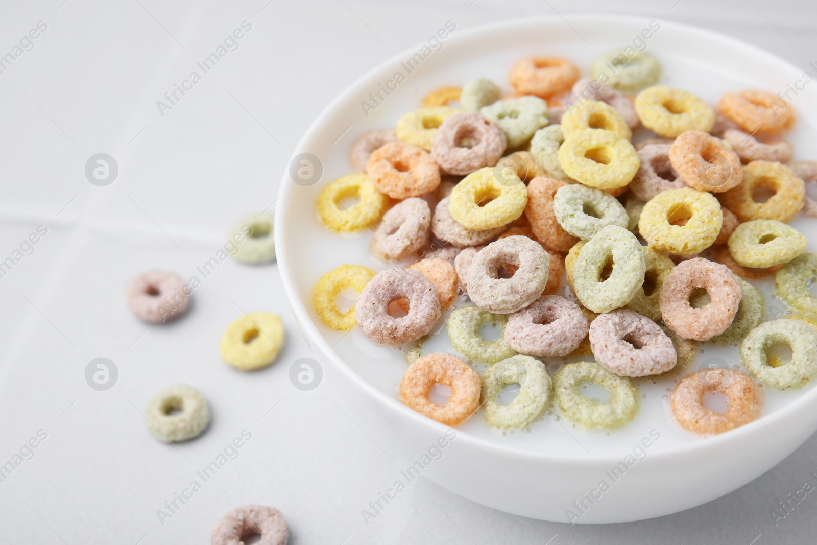 Photo of Cereal rings and milk in bowl on white tiled table, closeup. Space for text