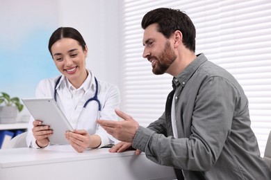 Photo of Doctor with tablet consulting patient during appointment in clinic