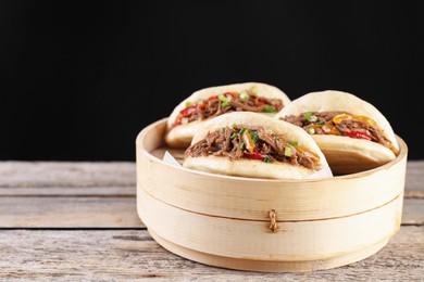 Photo of Delicious gua bao in bamboo steamer on wooden table. Space for text