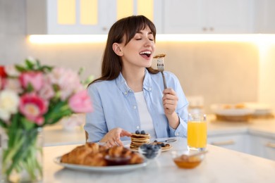 Photo of Smiling woman eating tasty pancakes at breakfast indoors