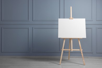 Photo of Wooden easel with blank canvas near grey wall indoors. Space for text