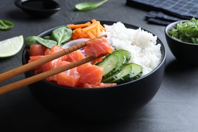 Photo of Wooden chopsticks with piece of salmon over delicious poke bowl on grey table, closeup