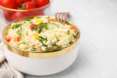 Photo of Cooked bulgur with vegetables in bowl on white tiled table, closeup. Space for text