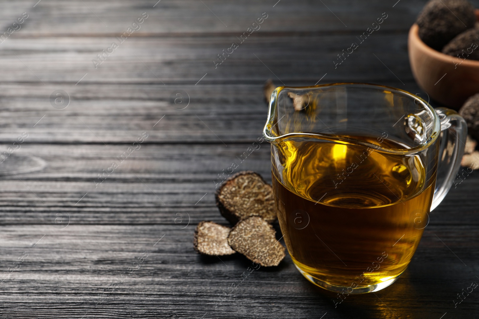 Photo of Fresh truffle oil in glass jug on black wooden table, space for text
