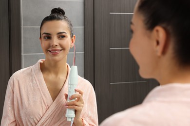 Photo of Woman using high frequency darsonval device near mirror in bathroom