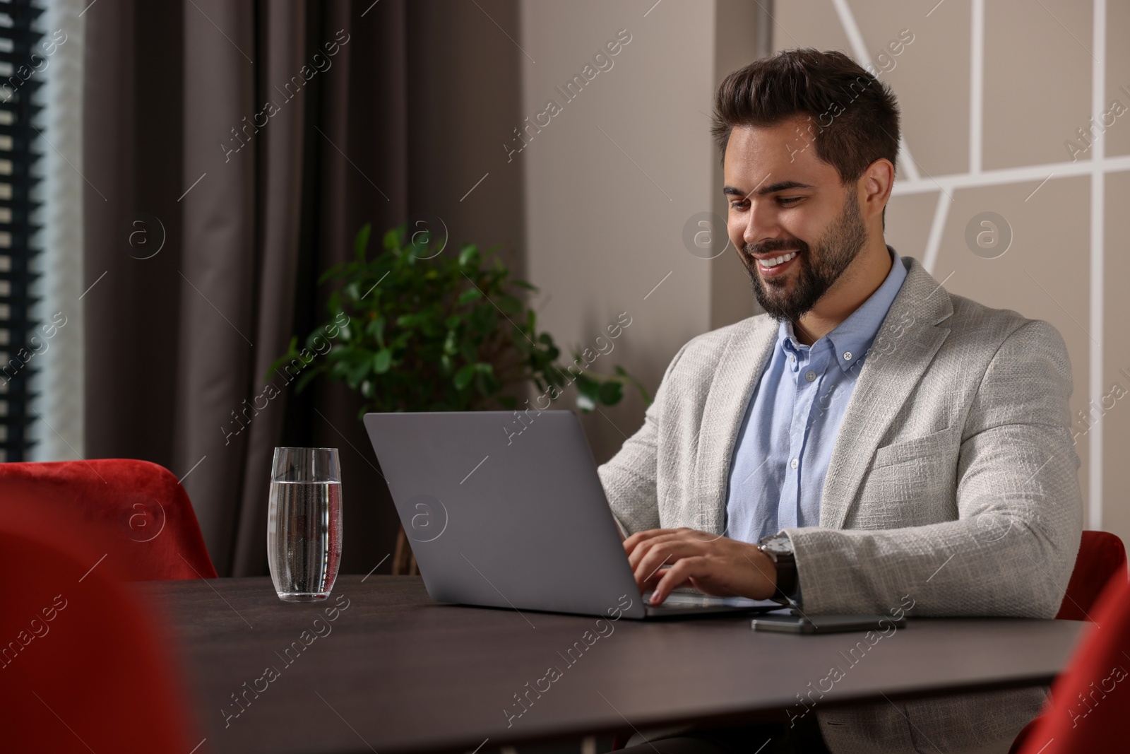 Photo of Happy young man working on laptop at table in office