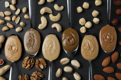 Photo of Tasty nut butters in spoons and raw nuts on dark gray table, flat lay