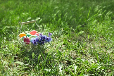 Photo of Basket with colorful Easter eggs and flowers on grass