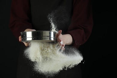 Photo of Woman sieving flour against black background, closeup