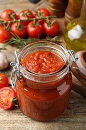 Photo of Homemade tomato sauce in jar and fresh ingredients on wooden table, closeup
