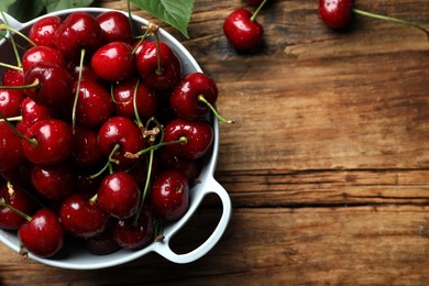 Photo of Wet red cherries in colander on wooden table, flat lay. Space for text