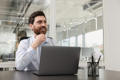 Photo of Man working on laptop at black desk in office. Space for text