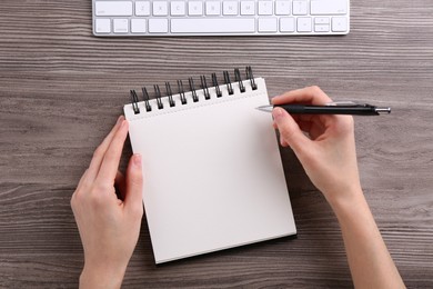 Photo of Woman writing in notebook at wooden table, top view