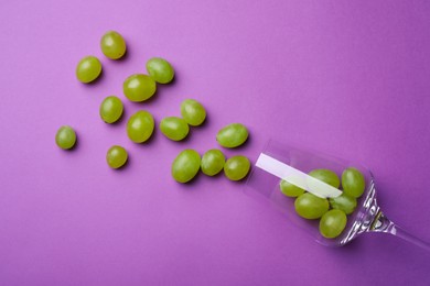 Photo of Wineglass with scattered grapes on violet background, flat lay