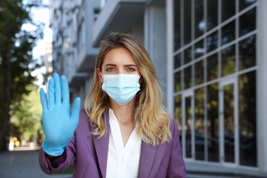 Photo of Woman in protective face mask showing stop gesture outdoors. Prevent spreading of coronavirus