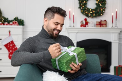 Photo of Happy young man opening Christmas gift at home