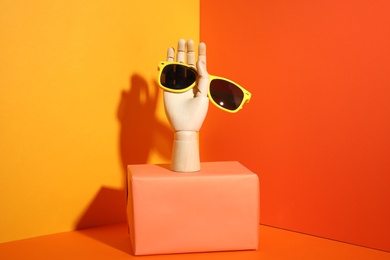 Photo of Wooden mannequin hand with stylish sunglasses on color background