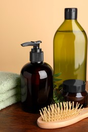 Photo of Bottles of shampoo, hairbrush and stacked towel on wooden table near beige wall, closeup