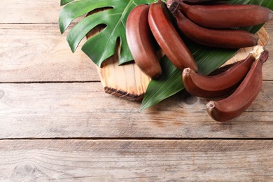 Delicious red baby bananas on wooden table, flat lay. Space for text