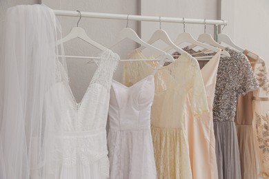 Photo of Hangers with different beautiful dresses and wedding veil on rack in atelier