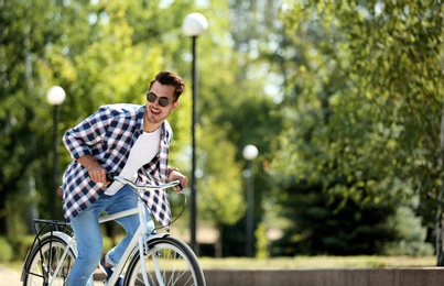 Photo of Handsome young hipster man riding bicycle in park